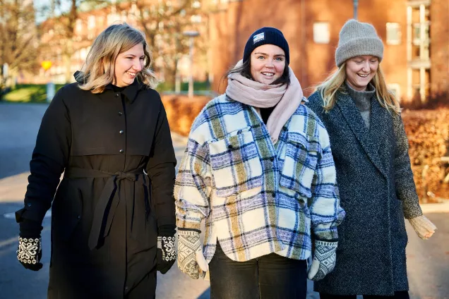 Three students dressed in winter attire walk in front of red brick buildings, photography by Johan Persson.