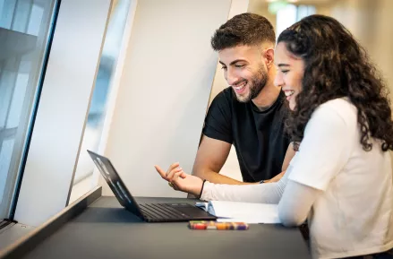 Två studenter diskuterar vid en laptop på ett ståbord. Fotograf Johan Persson.