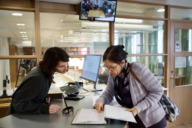 Bibliotekarie och forskare står vid informationsdisk och tittar i en pärm tillsammans. Fotograf Johan Bävman.