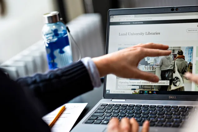 En öppen laptop. Händer som pekar mot skärmen.